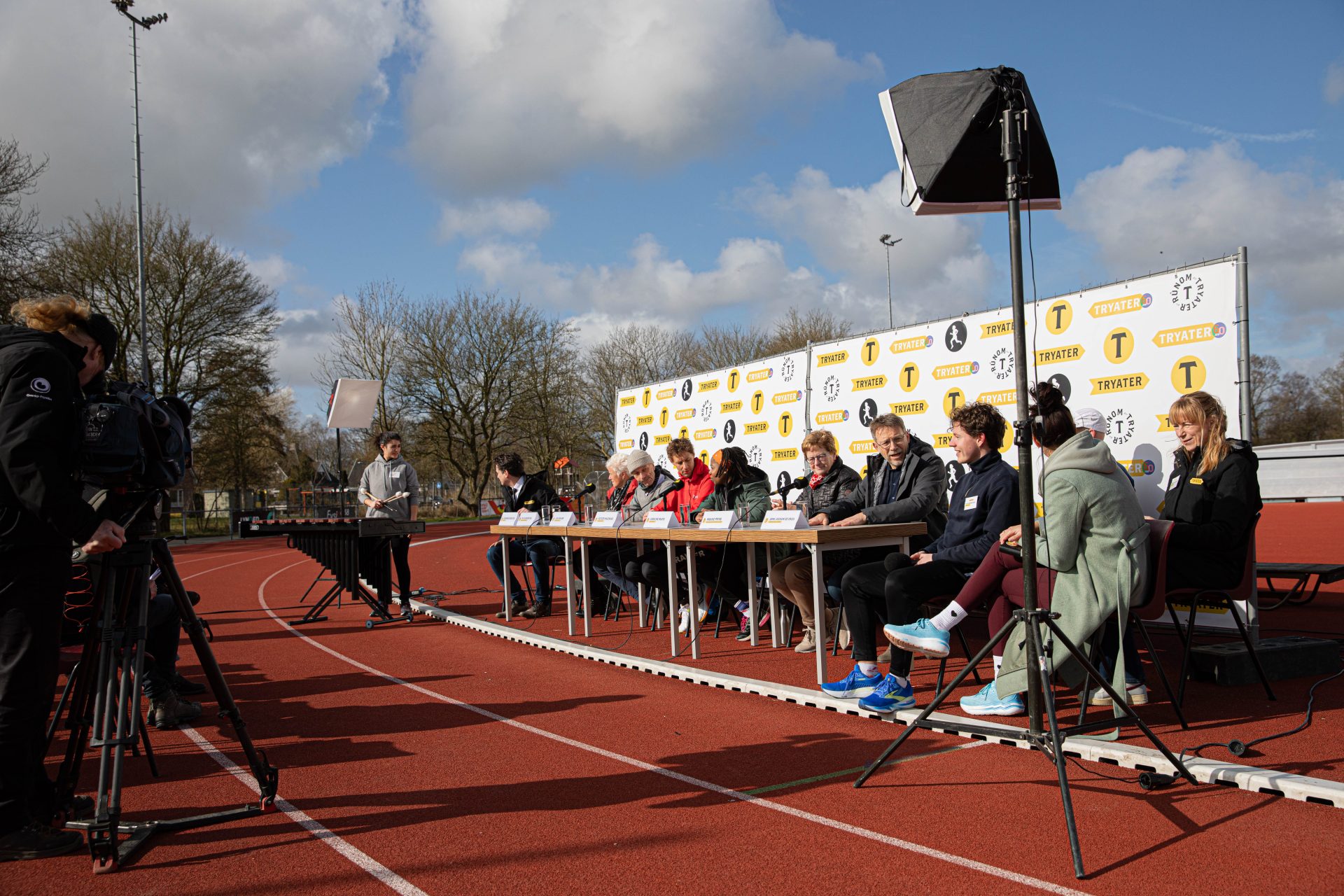 foto van 7 personen achter een persconferentietafel op de atletiekbaan