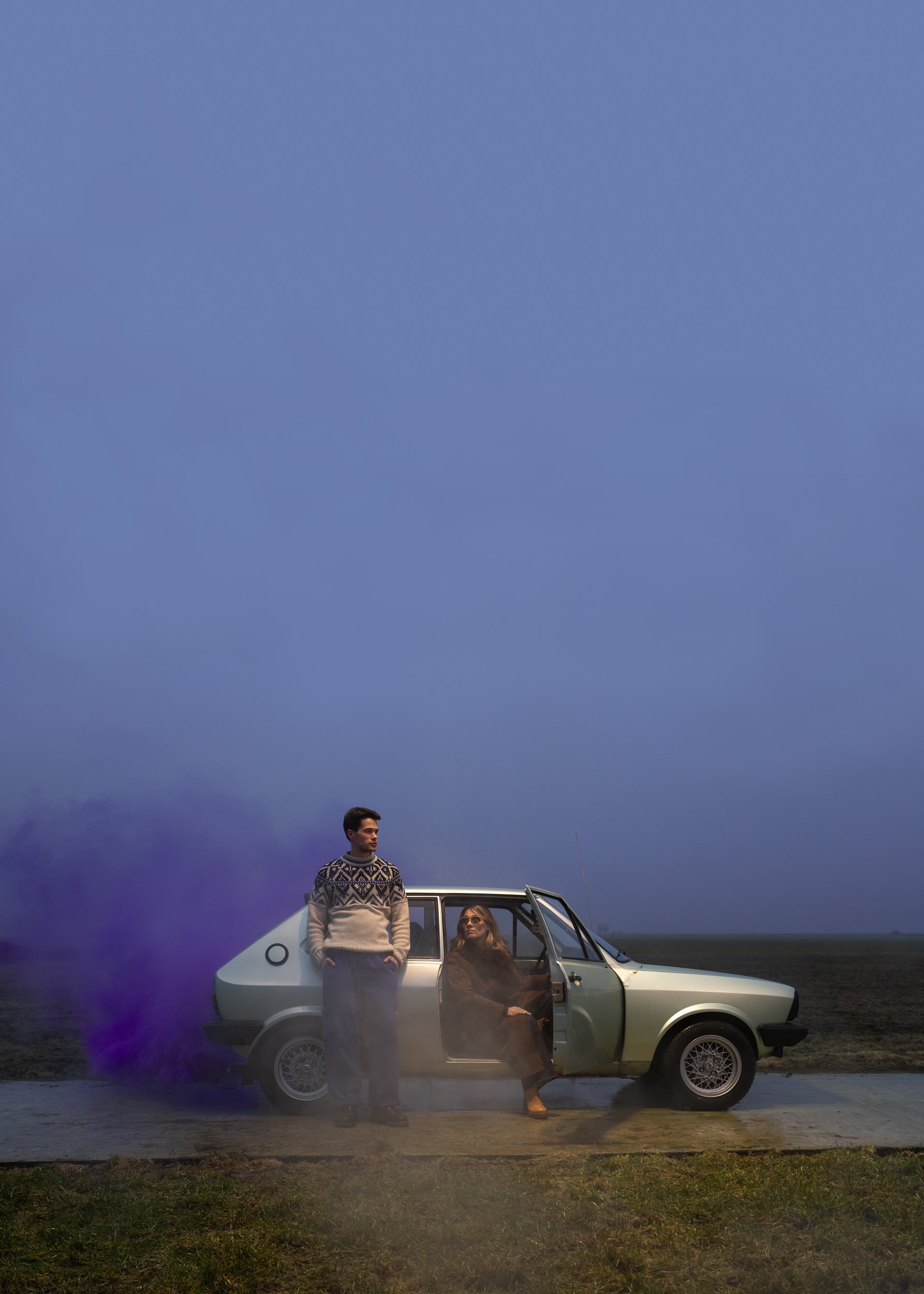 Foto met een stilstaande auto met paarse rook en twee personen